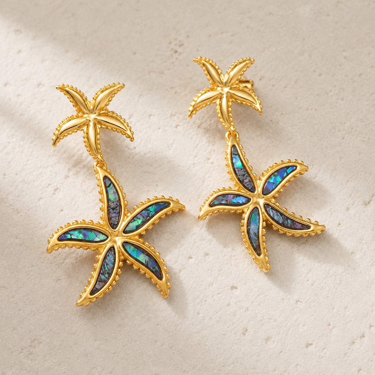 Gold starfish earrings with multicolored stone centers on a beige background