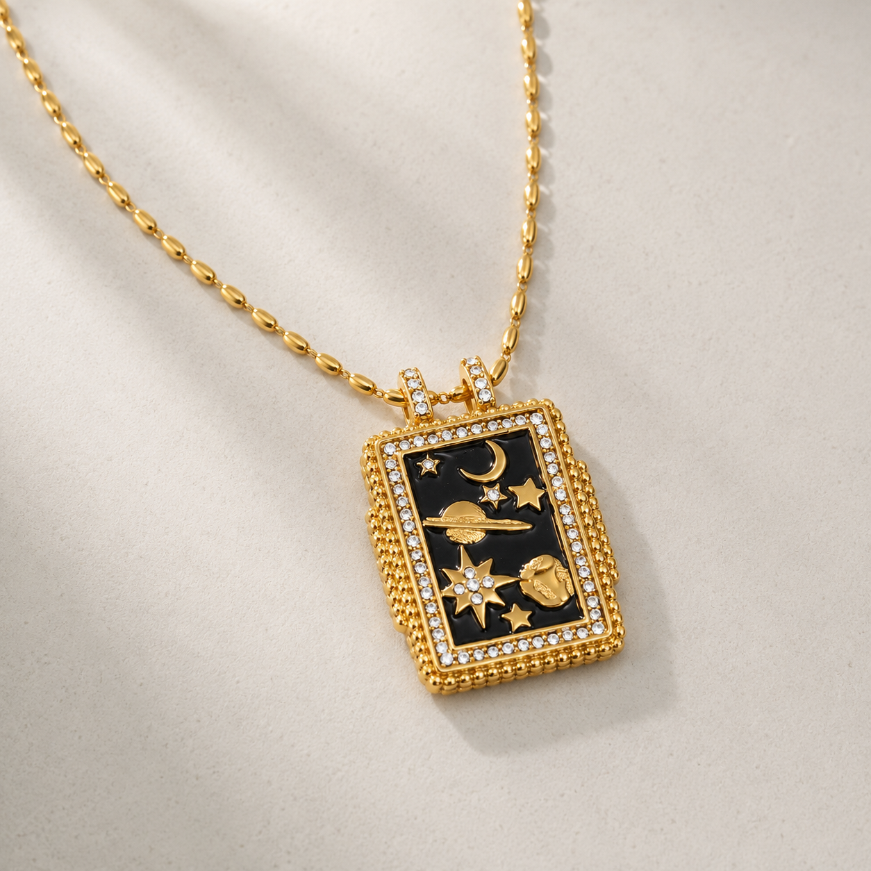 Gold necklace with a black pendant featuring celestial designs on a beige background