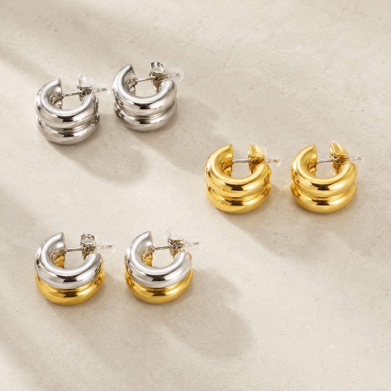 Pair of silver hoop earrings and gold hoop earrings on a beige background