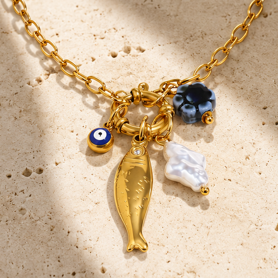 Gold fish charm necklace with evil eye, pearl and blue flower accents on an 18K gold-plated O-link chain.