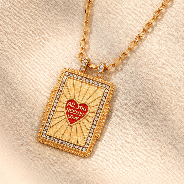 18K gold plated stainless steel rectangular pendant necklace with red heart saying All You Need Is Love, sunburst detail and crystal-style border.