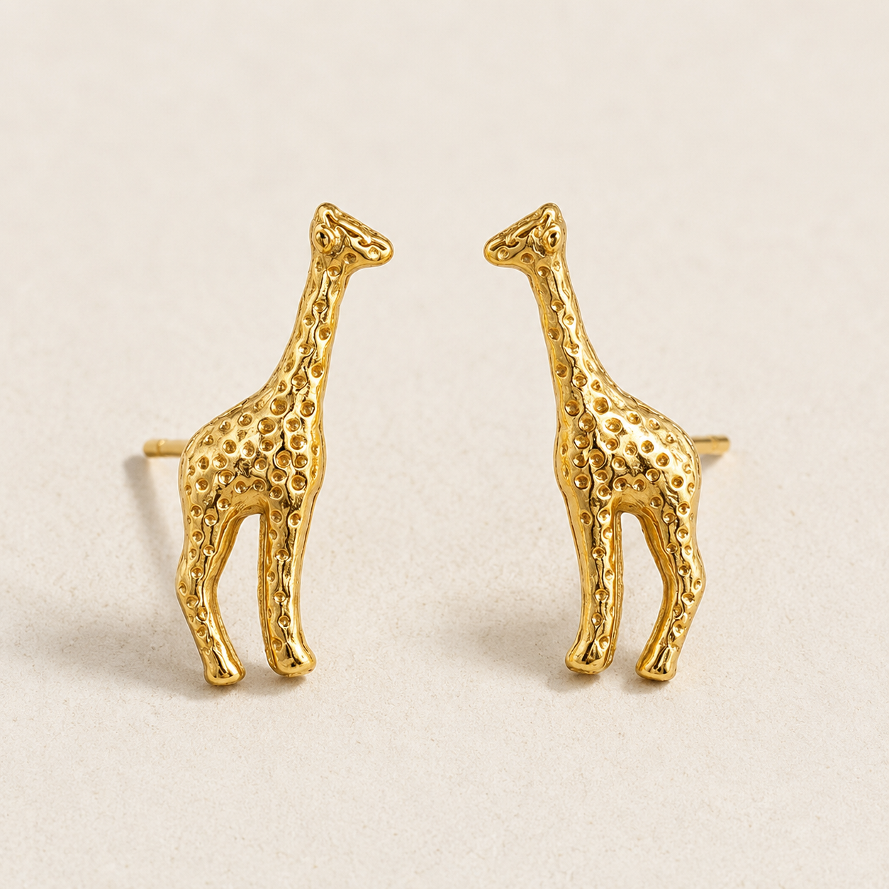 Gold giraffe-shaped earrings on a beige background