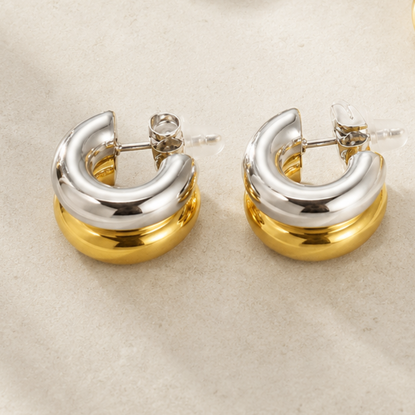 Pair of gold and silver hoop earrings on a beige background