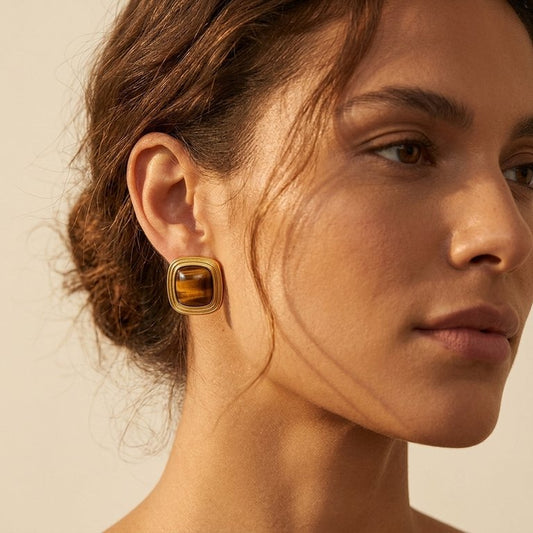 Close-up of a woman wearing a gold earring with a brown gemstone on a beige background